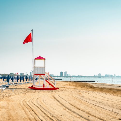 Beach at the Adriatic sea coastline in Italy, Europe during summer. Traditional hut for the beach lifeguard and a red flag.