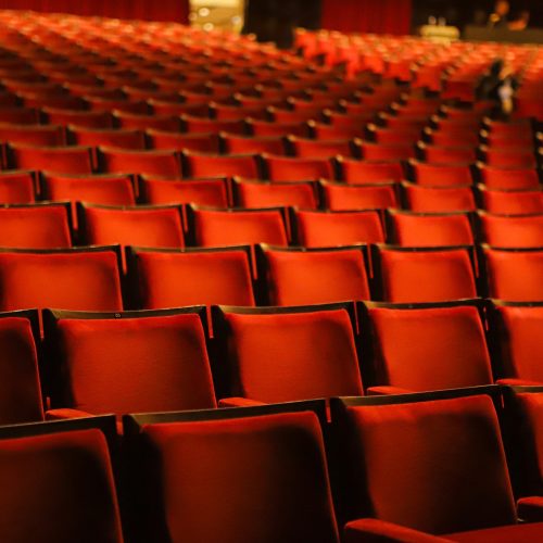 Velvety red chairs in a theater, with continuity of lines and numbers (unidentifiable) on top.
