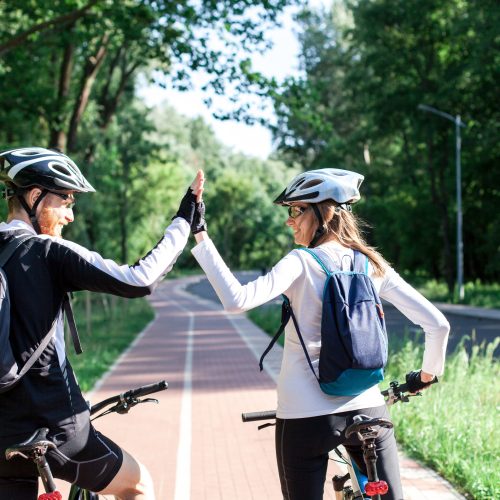 Cyclists riding bikes. Happy couple in protective helmets having fun on bicycle path. Safety, ecological, healthy lifestyle. Sport activity outdoors in nature. High-fives gesture, green initiatives.